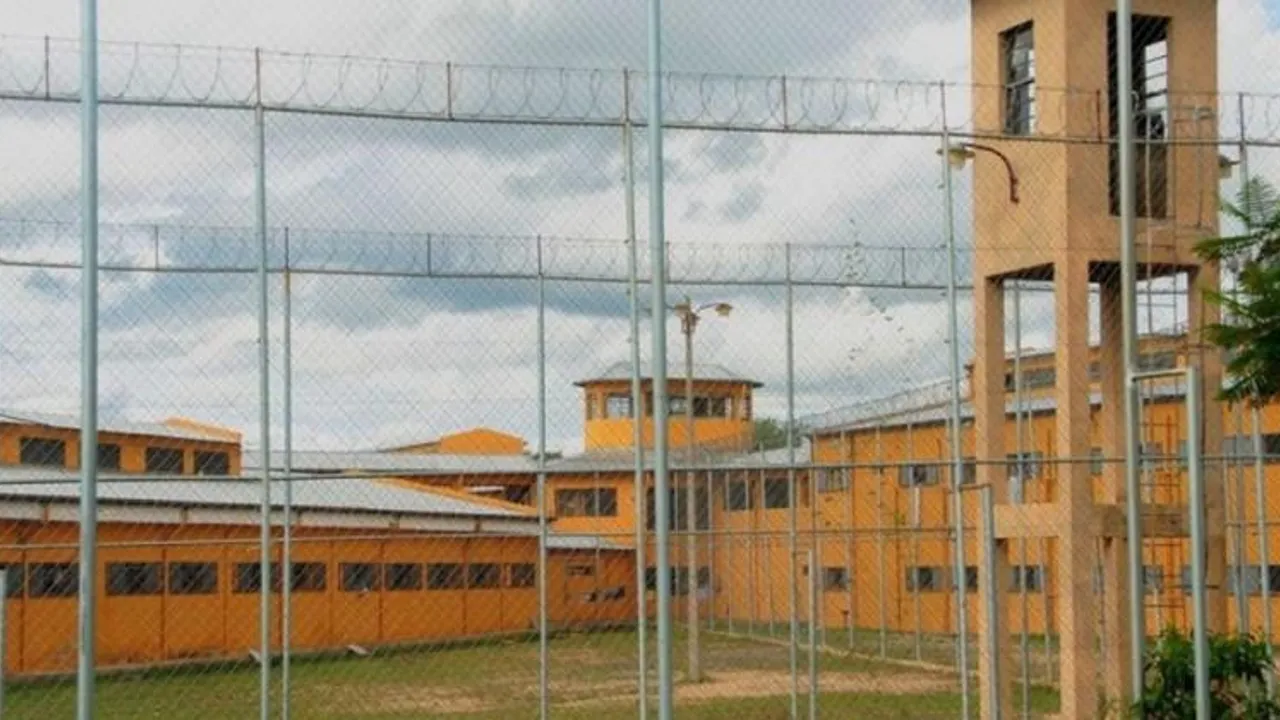 Alambrado perimetral y torre de vigilancia frente a los pabellones anaranjados de una penitenciaría.