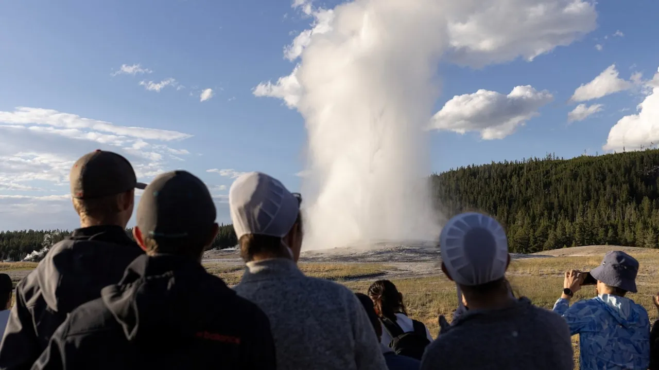 Grupo de visitantes observa a distancia una columna de vapor emergiendo de un géiser en un día despejado