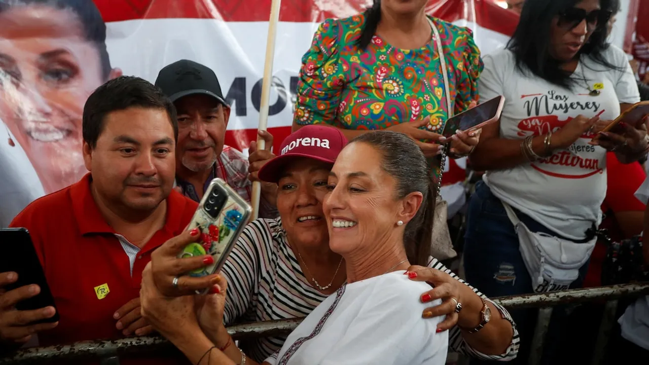 Claudia Sheinbaum sonríe mientras se toma una autofoto con simpatizantes que llevan gorras y carteles partidarios.
