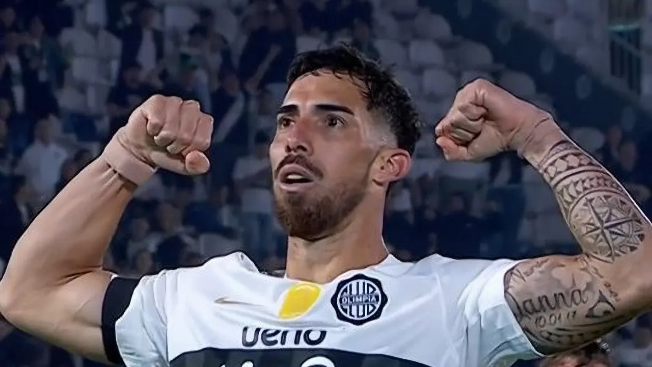 Futbolista de Olimpia con camiseta blanca festeja con ambos brazos flexionados hacia arriba en el estadio.