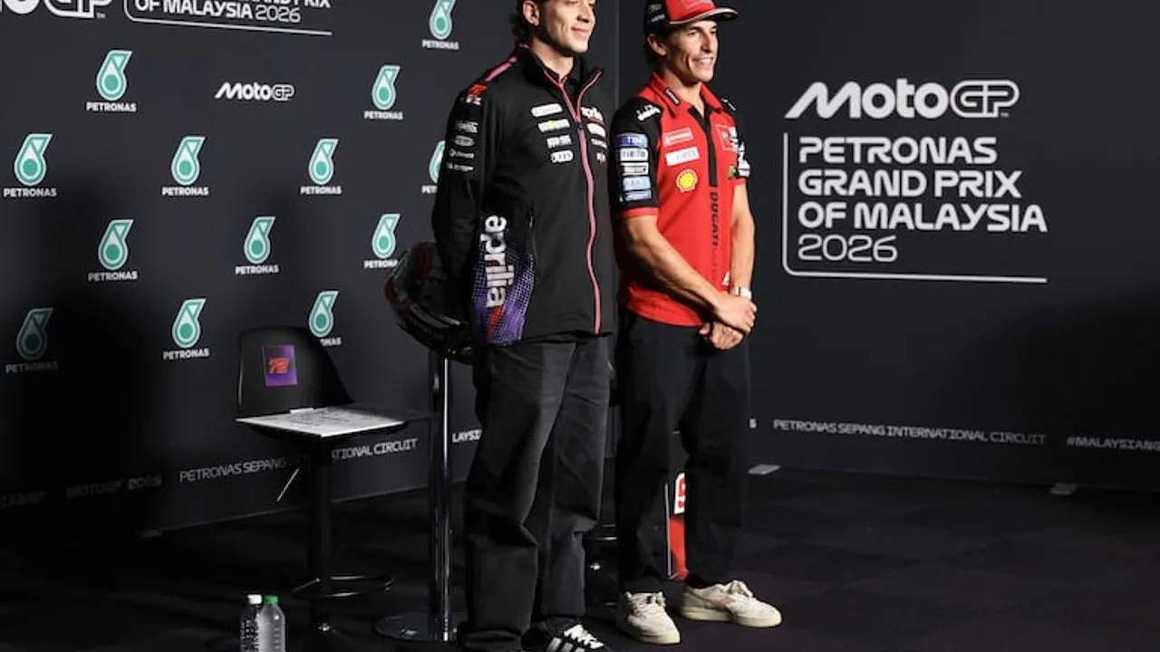 Marco Bezzecchi y Marc Márquez de pie en una sala de prensa ante paneles oficiales del Gran Premio de Malasia