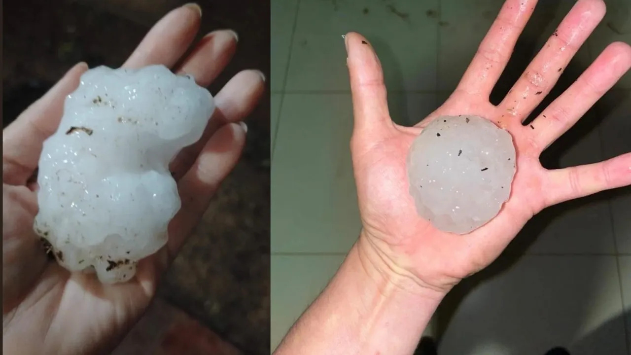 Dos manos abiertas sostienen enormes trozos de hielo blanco caídos durante un temporal severo.