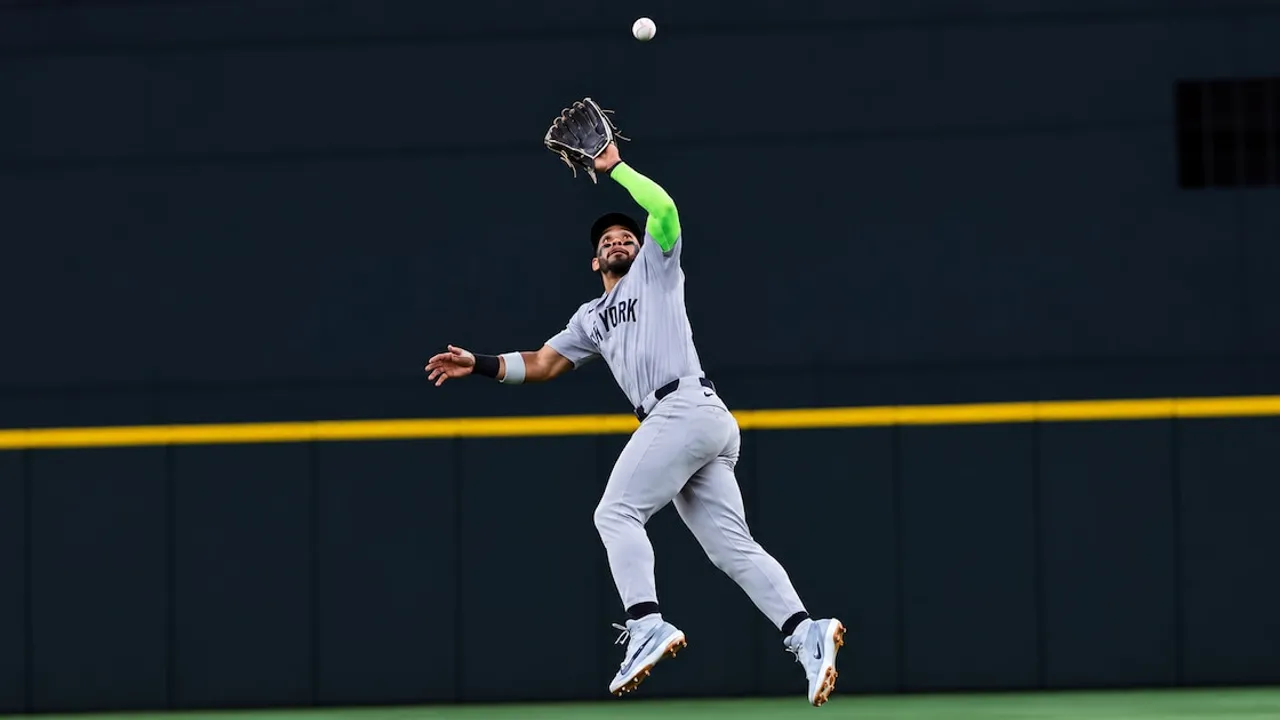 Pelotero de béisbol con uniforme de Nueva York salta con el guante extendido hacia arriba para atrapar una pelota.
