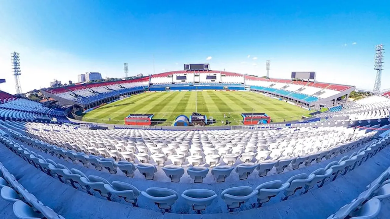 Vista panorámica del Estadio Defensores del Chaco con sus graderías vacías pintadas de azul, blanco y rojo bajo un cielo despejado.