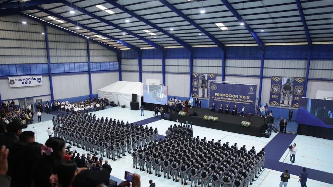 Cientos de agentes penitenciarios formados en filas dentro de un polideportivo frente al escenario principal.