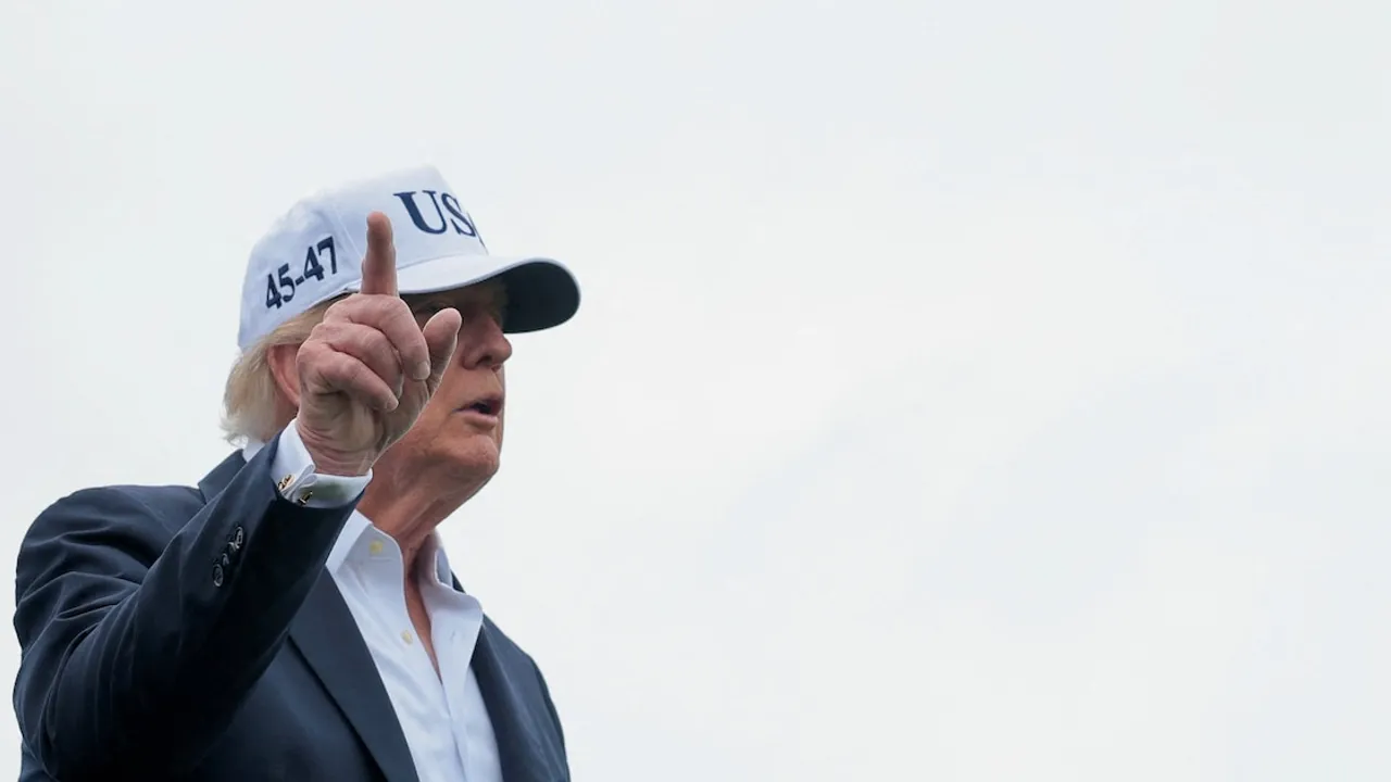 Donald Trump con gorra blanca señalando hacia arriba con el dedo índice al aire libre.
