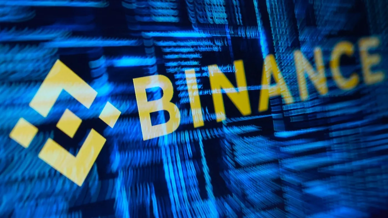 Logotipo de Binance en letras amarillas sobre una pantalla azul con código de programación informático.