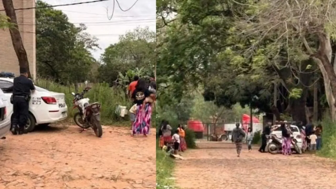 Agentes policiales y vecinos se congregan cerca de una patrullera en una calle de tierra rodeada de árboles.