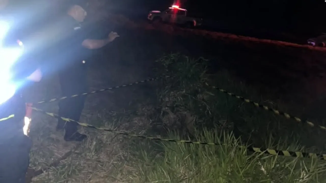 Agentes policiales acordonan con cinta perimetral un terreno con malezas de noche junto a una patrullera.