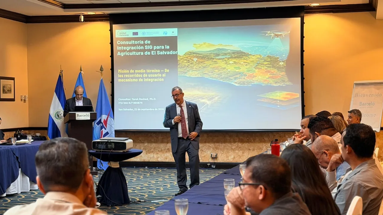 Expositor con micrófono ante una pantalla sobre sistemas geográficos y público sentado en una conferencia.