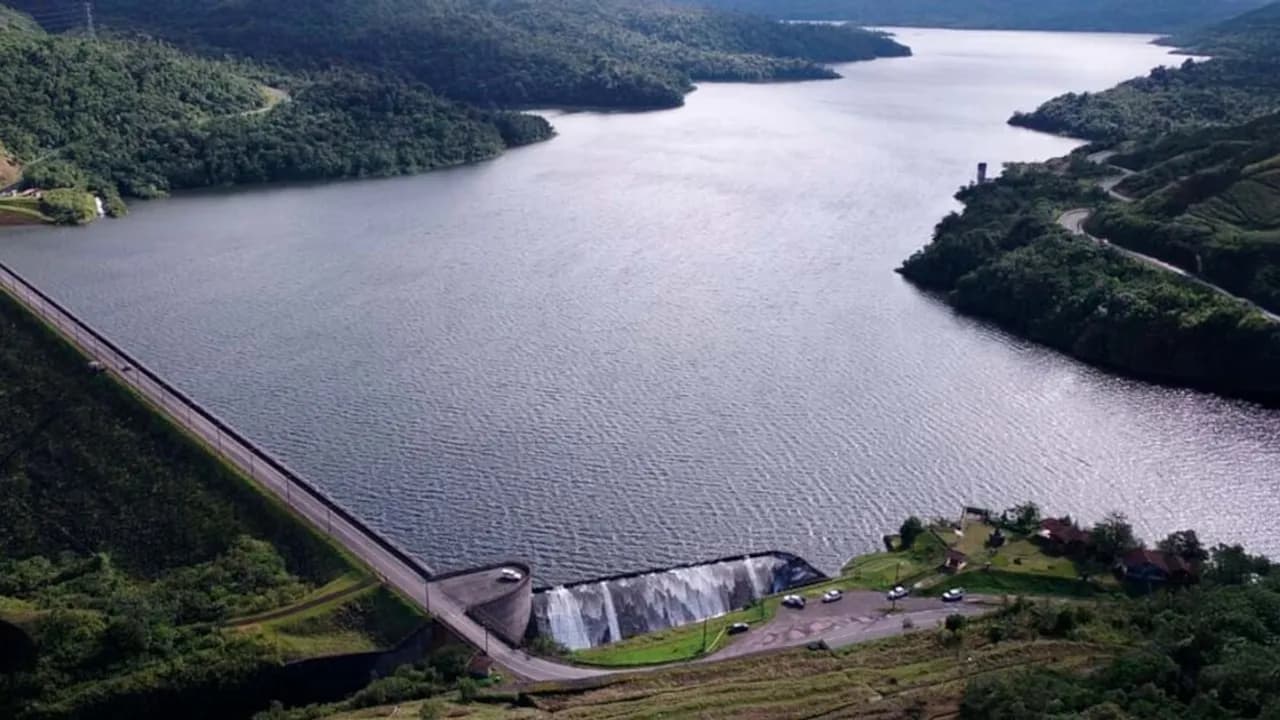 Vista aérea de una gran represa e hidroeléctrica rodeada de montañas verdes y agua.