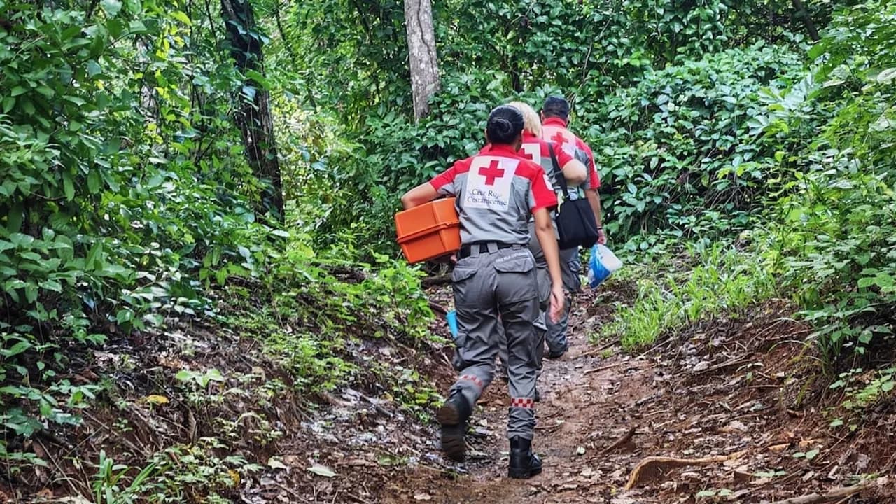 Rescatistas de la Cruz Roja Costarricense caminan por un sendero boscoso con equipo de emergencia en mano.