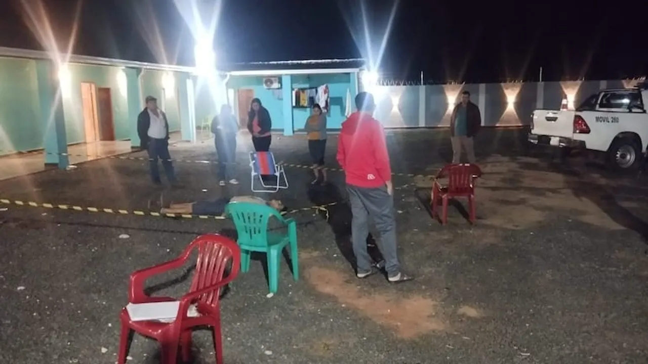 Efectivos policiales y personas acordonan la escena de un crimen nocturno en el patio de un hospedaje