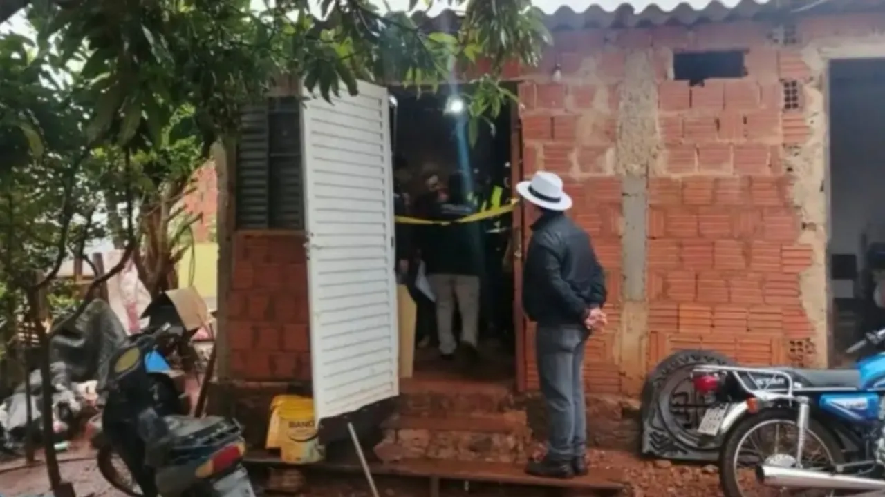 Agentes policiales y un perito inspeccionan el acceso de una casa de ladrillos con cinta perimetral.