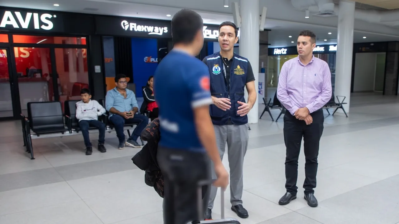 Funcionarios gubernamentales dialogan con un viajero con maleta en el hall de un aeropuerto