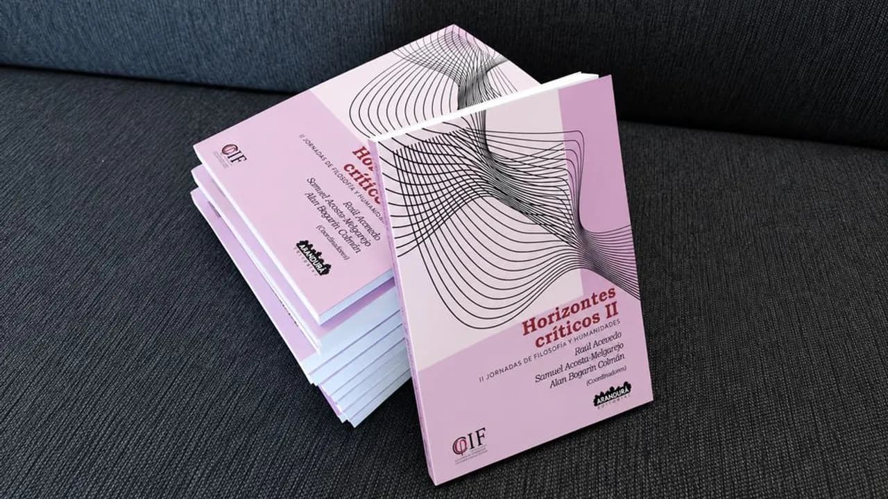 Varios ejemplares impresos del libro Horizontes Críticos II apilados sobre una superficie de tela gris oscura.