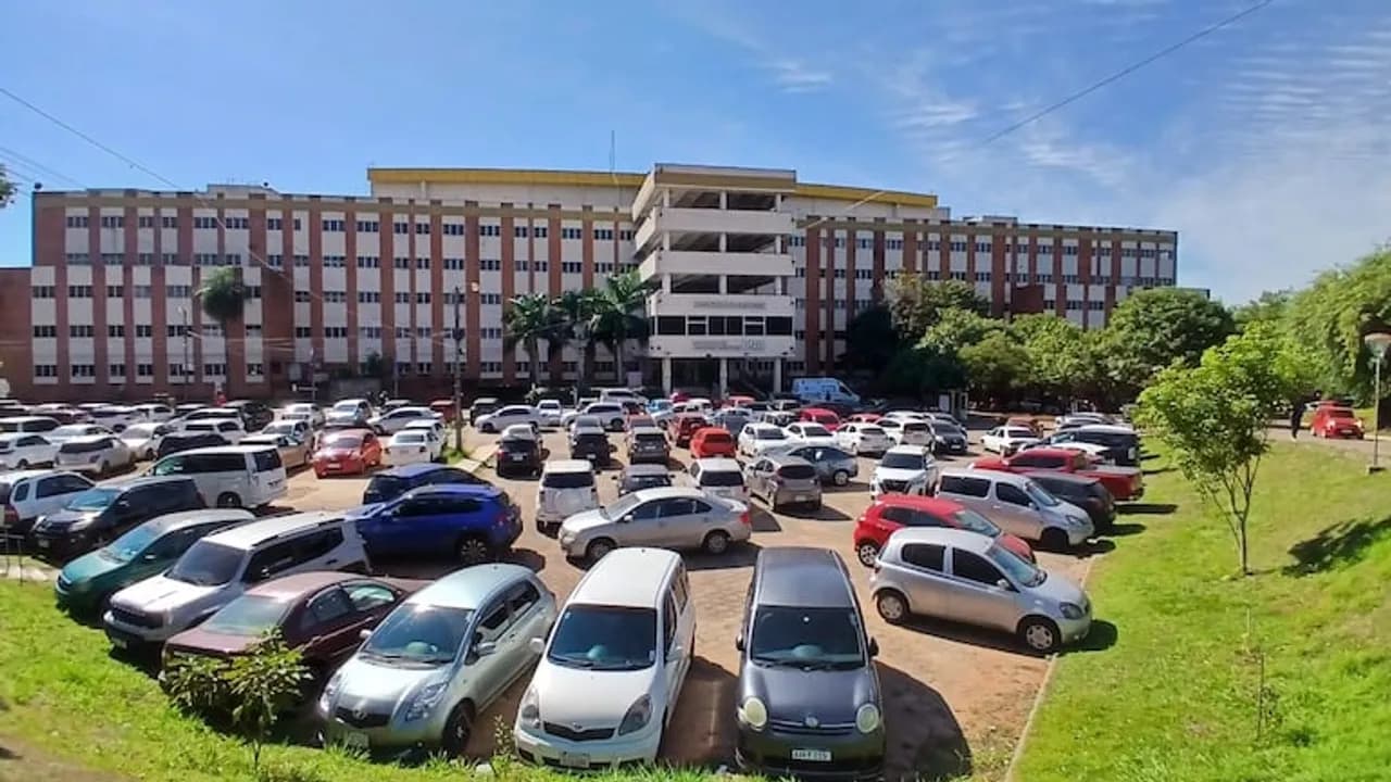 Edificio del Hospital de Clínicas con amplio estacionamiento de vehículos en el frente bajo el sol