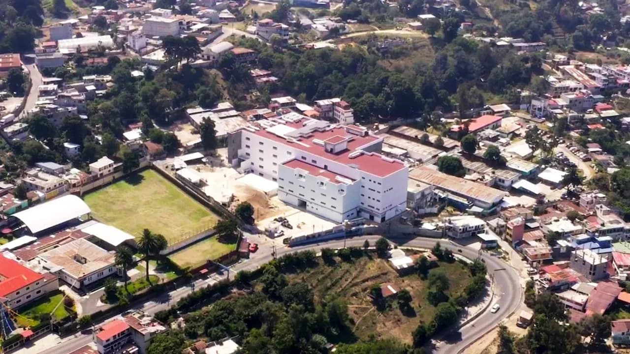 Vista aérea de un moderno edificio hospitalario blanco de varios pisos rodeado de vegetación y viviendas.