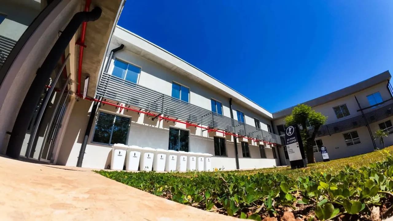 Patio interno y fachada de dos plantas del nuevo albergue hospitalario con césped y contenedores blancos