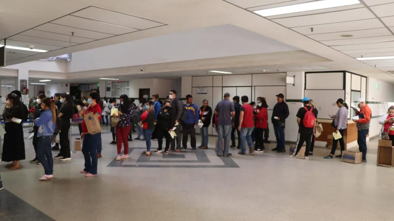 Fila de personas esperando atención médica en el amplio pasillo de un centro hospitalario público.