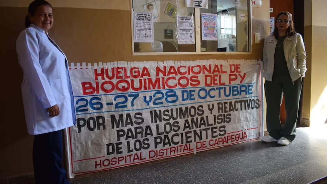 Dos trabajadoras posan junto a un cartel de huelga en el pasillo del Hospital Distrital de Carapeguá.