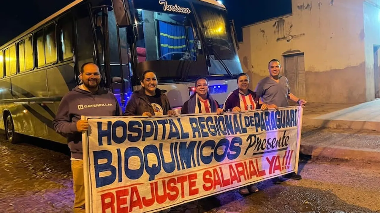 Grupo de profesionales bioquímicos sosteniendo una pancarta de protesta frente a un ómnibus de noche