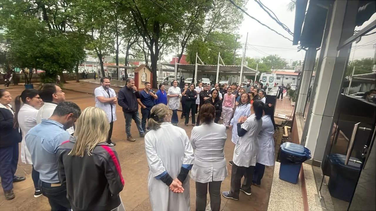 Grupo de profesionales de la salud vestidos con batas blancas reunidos en asamblea frente a un centro médico.