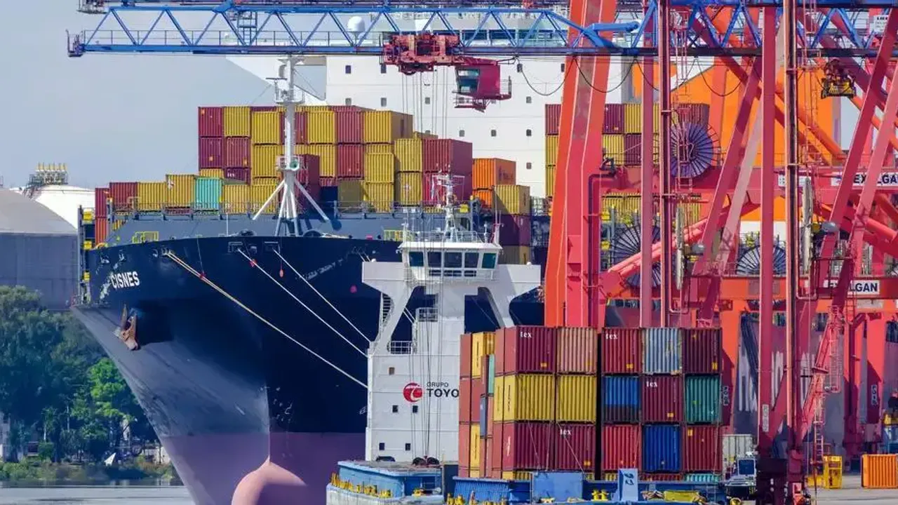 Un buque de carga repleto de contenedores junto a grúas portuarias en una terminal marítima.