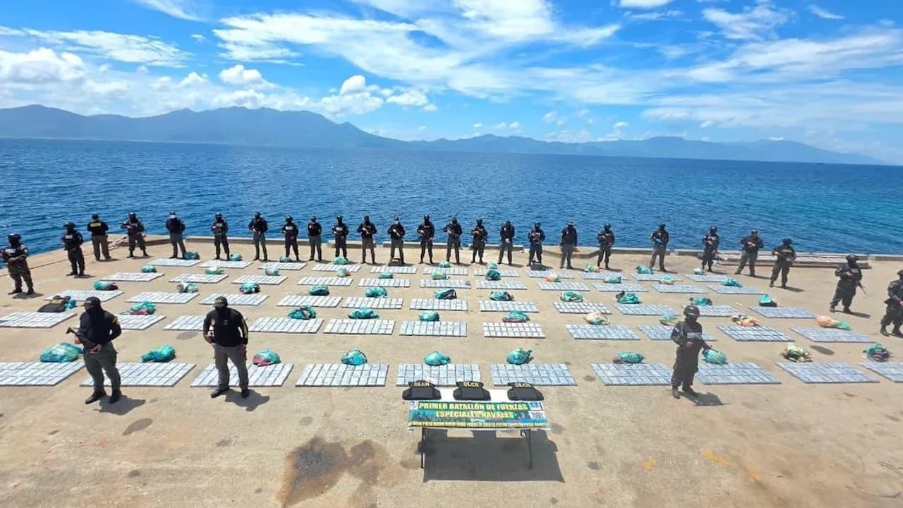 Agentes armados custodian decenas de paquetes de droga colocados en una cubierta frente al mar caribeño.