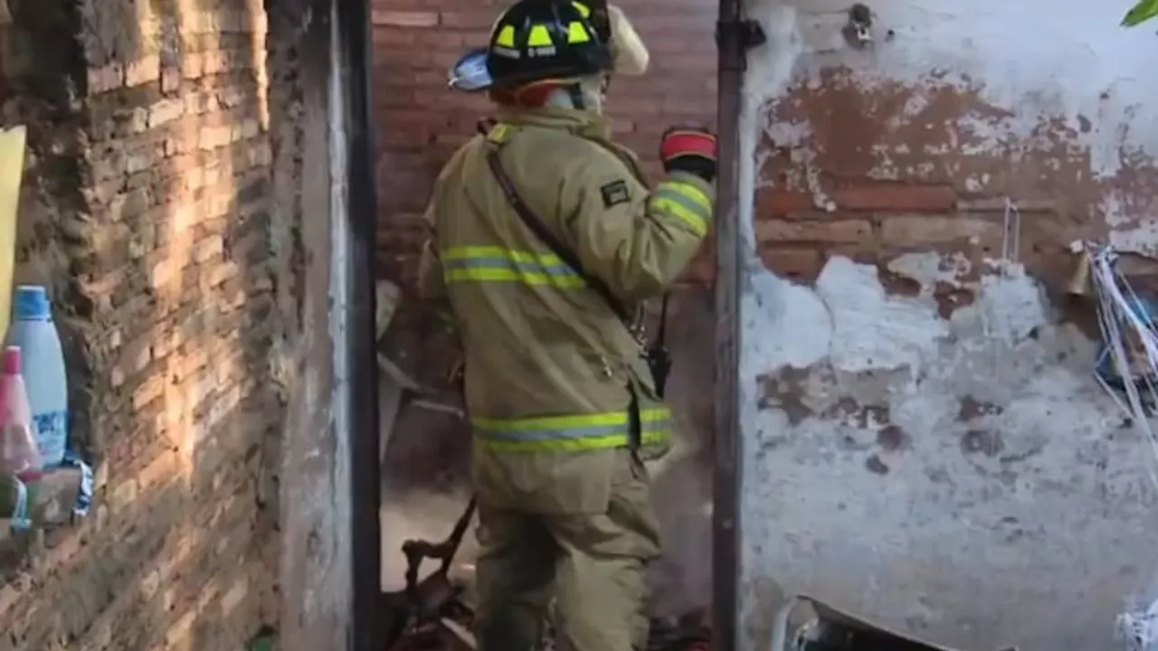 Bombero con traje de protección y casco de espaldas frente a la entrada de un edificio de ladrillos dañado.
