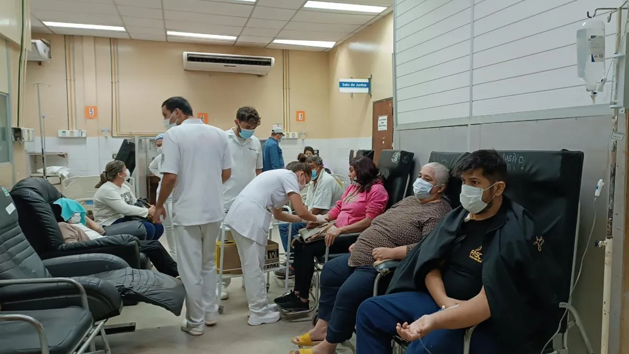 Pacientes con tapabocas reciben atención médica y suero en una sala de espera hospitalaria.
