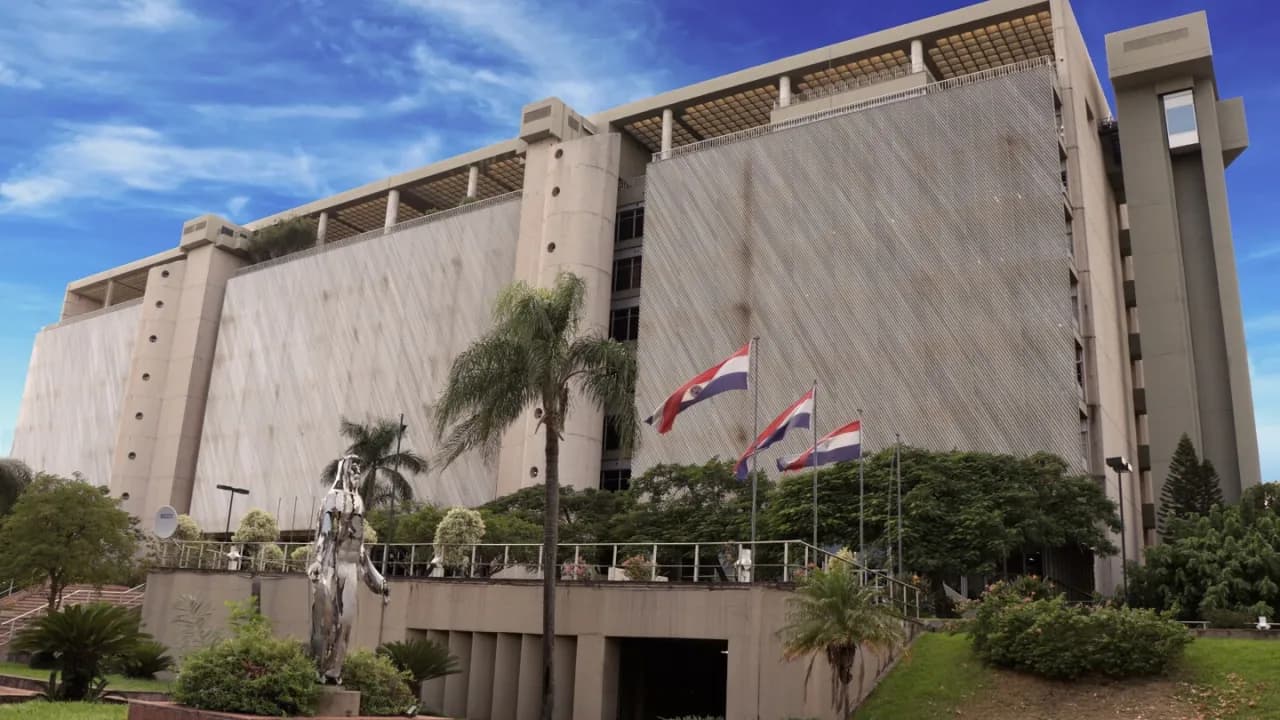Fachada del edificio del Banco Central del Paraguay con banderas nacionales y jardines en Asunción.