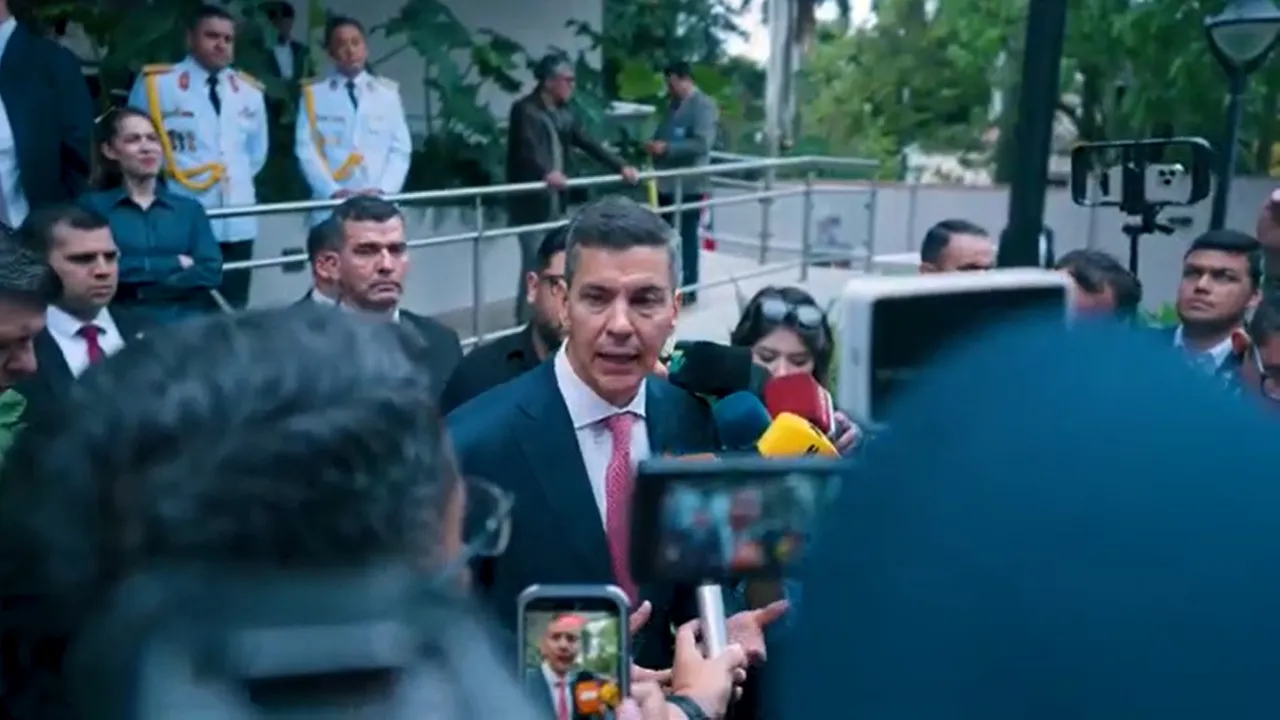 Santiago Peña con traje oscuro y corbata habla rodeado de micrófonos de prensa en un patio exterior con guardias.