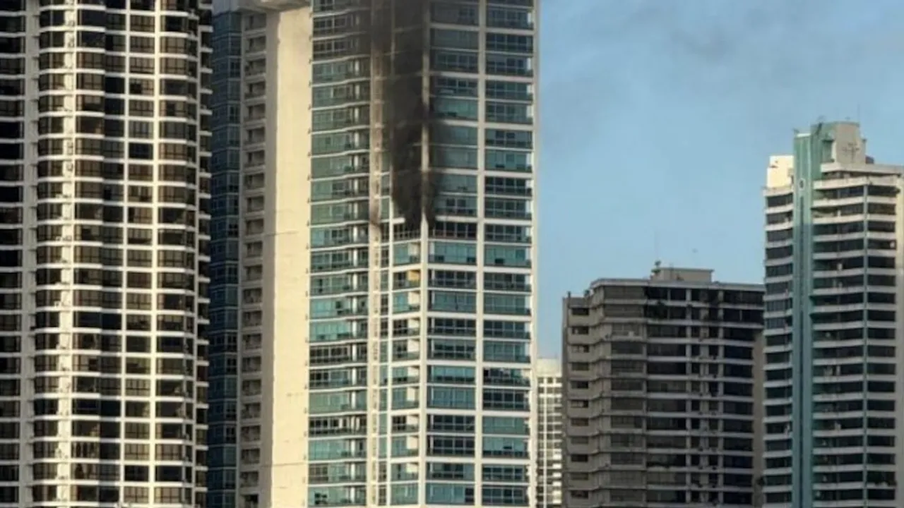 Columna de humo negro saliendo de un piso alto de un rascacielos residencial entre otros edificios urbanos.