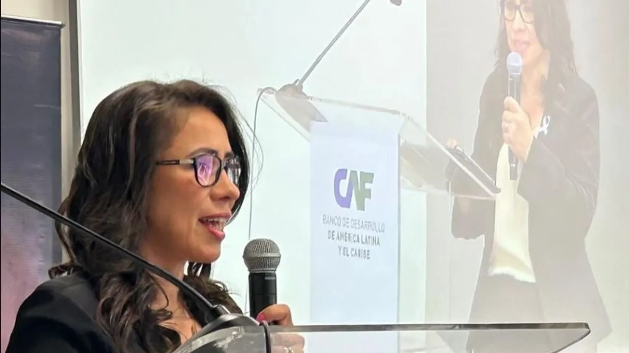 Una mujer con lentes habla frente a un podio con el logotipo del banco CAF y un micrófono en mano.