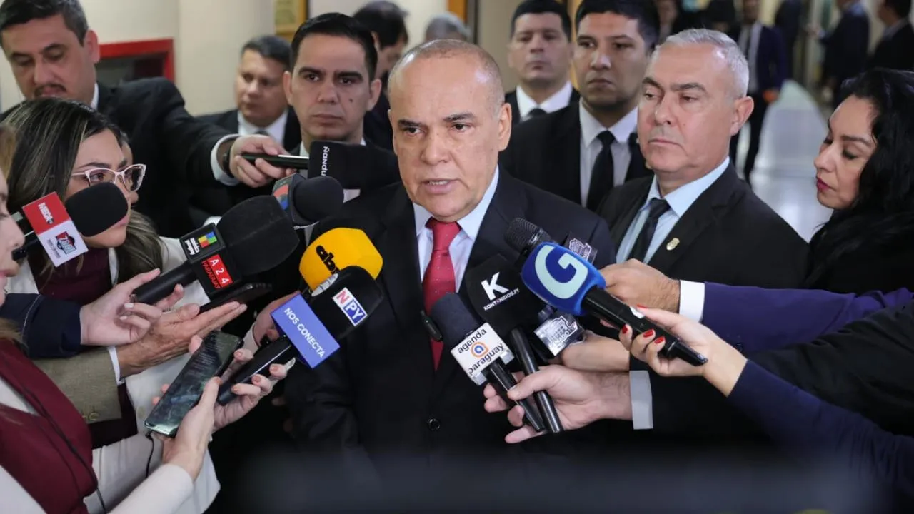 Basilio Núñez responde a las preguntas de periodistas rodeado por micrófonos y cámaras en un pasillo legislativo.