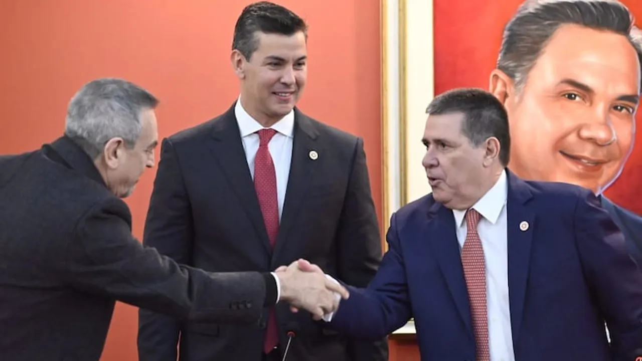 Dirigentes políticos vestidos con traje formal estrechan manos en un salón con un cuadro de fondo.