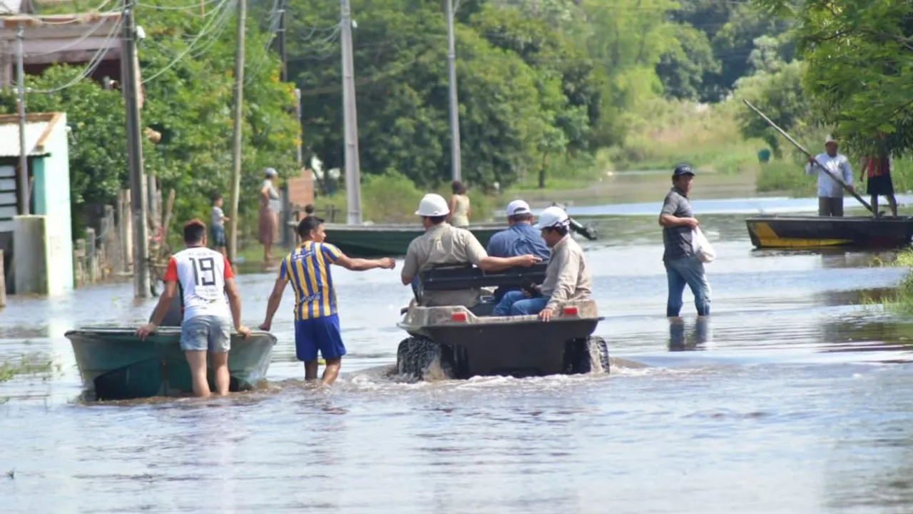 Vehículo anfibio y botes navegan por una calle completamente inundada donde varios pobladores caminan con el agua a la cintura.
