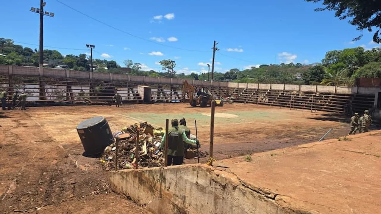 Trabajadores y maquinarias limpian restos de basura y barro acumulados en una cancha tras la crecida del río.