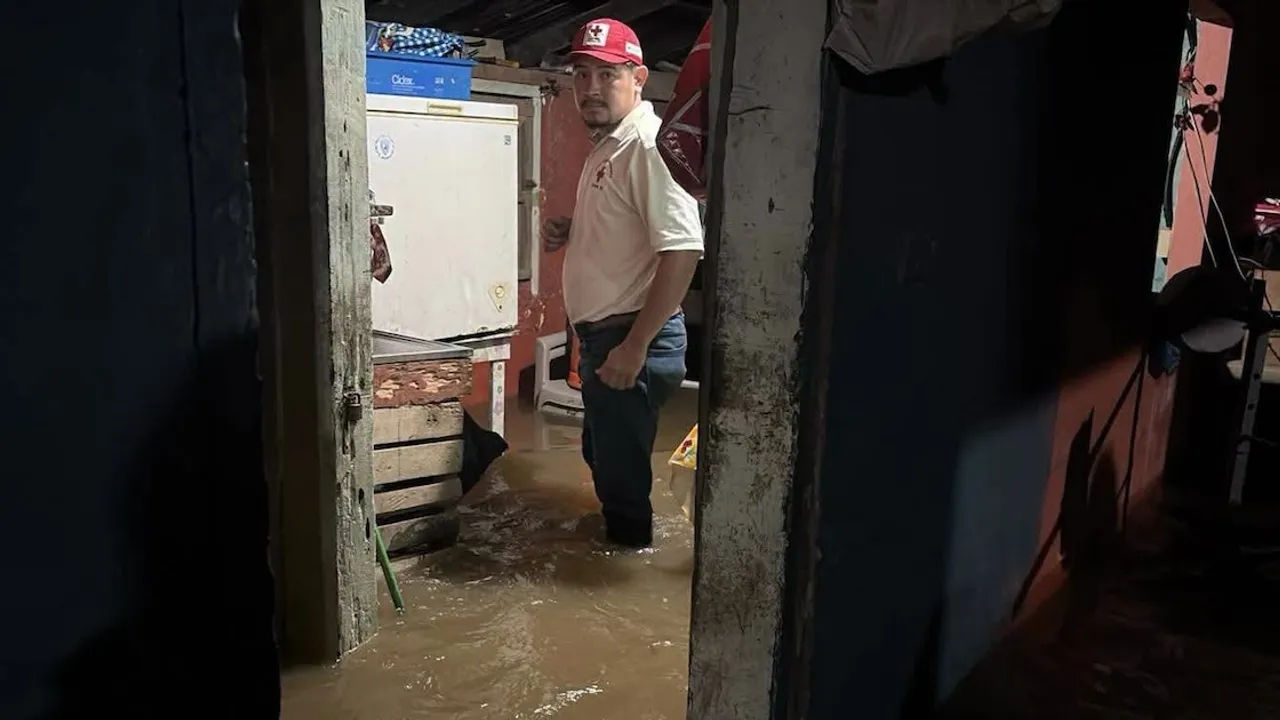 Hombre con gorra roja y camisa de voluntario parado con el agua hasta las rodillas dentro de una casa inundada