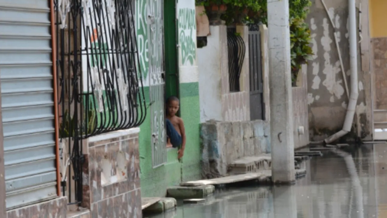 Un niño observa desde el umbral de una vivienda una calle totalmente anegada por el agua estancada.