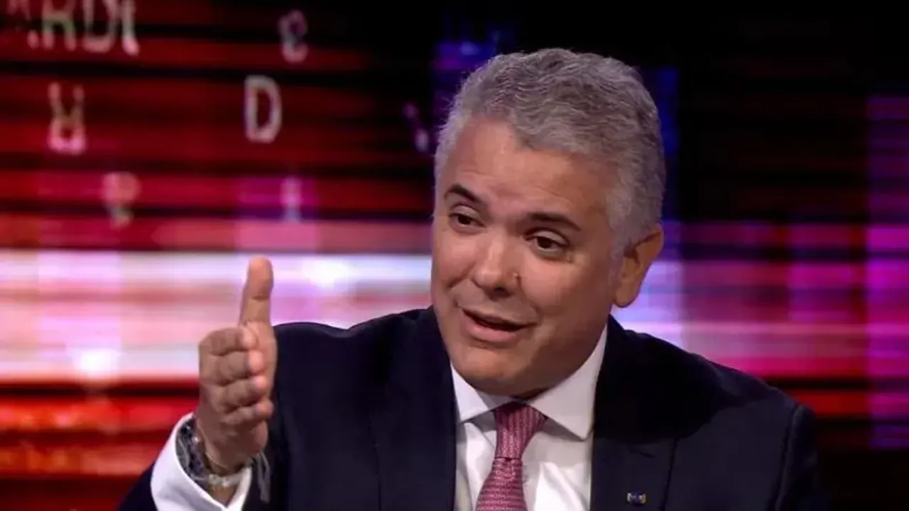 Hombre de traje oscuro y corbata gesticulando con la mano derecha abierta en un set televisivo