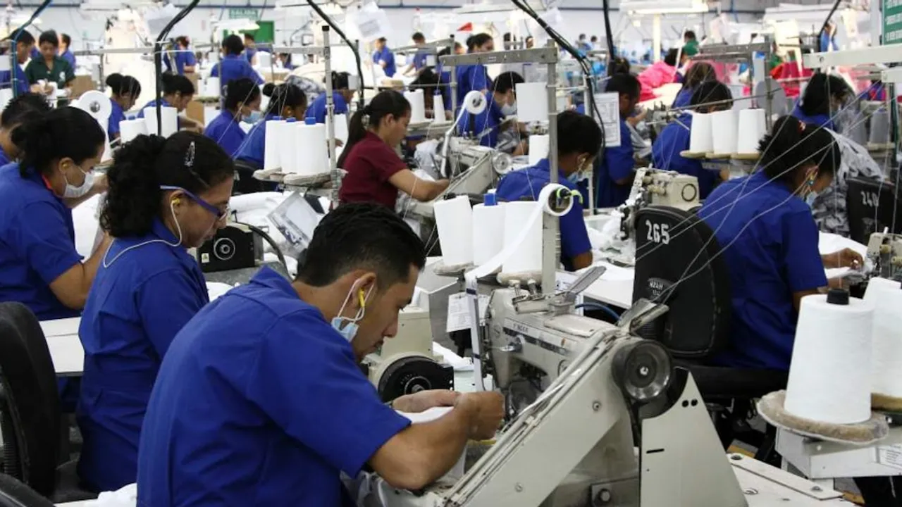 Operarios con uniforme azul trabajan en máquinas de coser dentro de una nave industrial de confección textil.