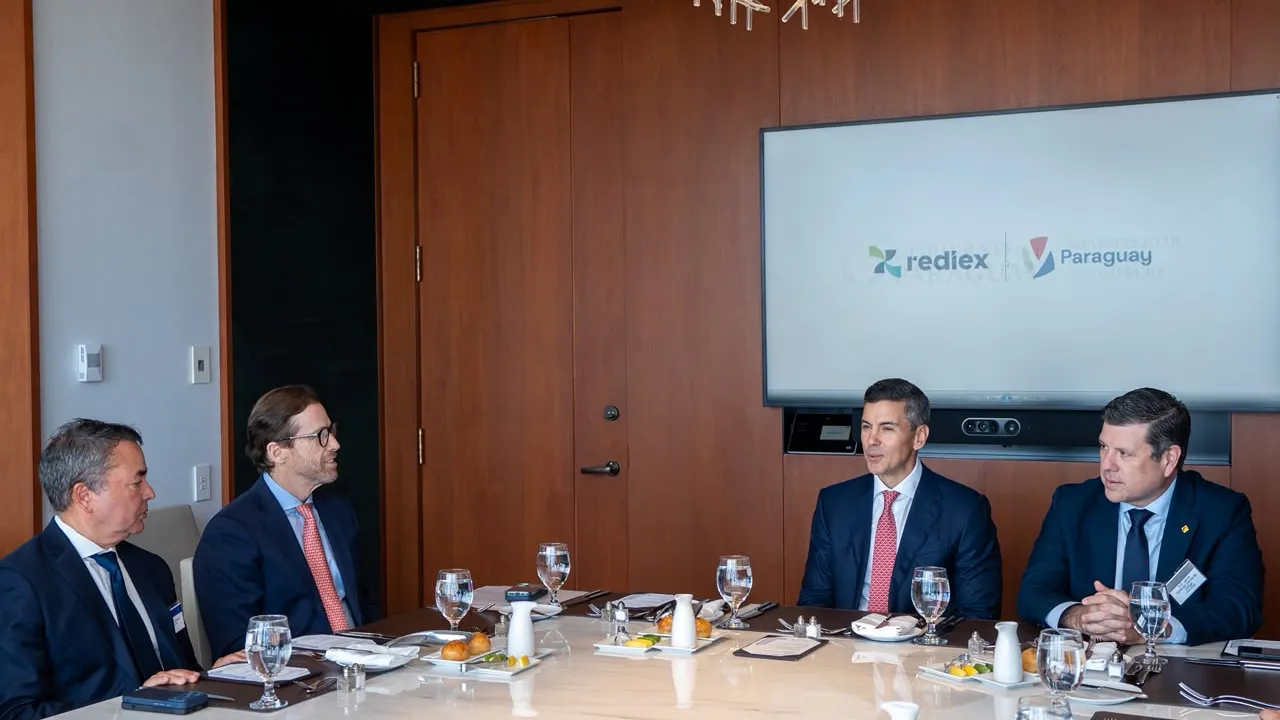 Santiago Peña y miembros de su comitiva conversan en una mesa de reuniones ante una pantalla institucional en Nueva York.