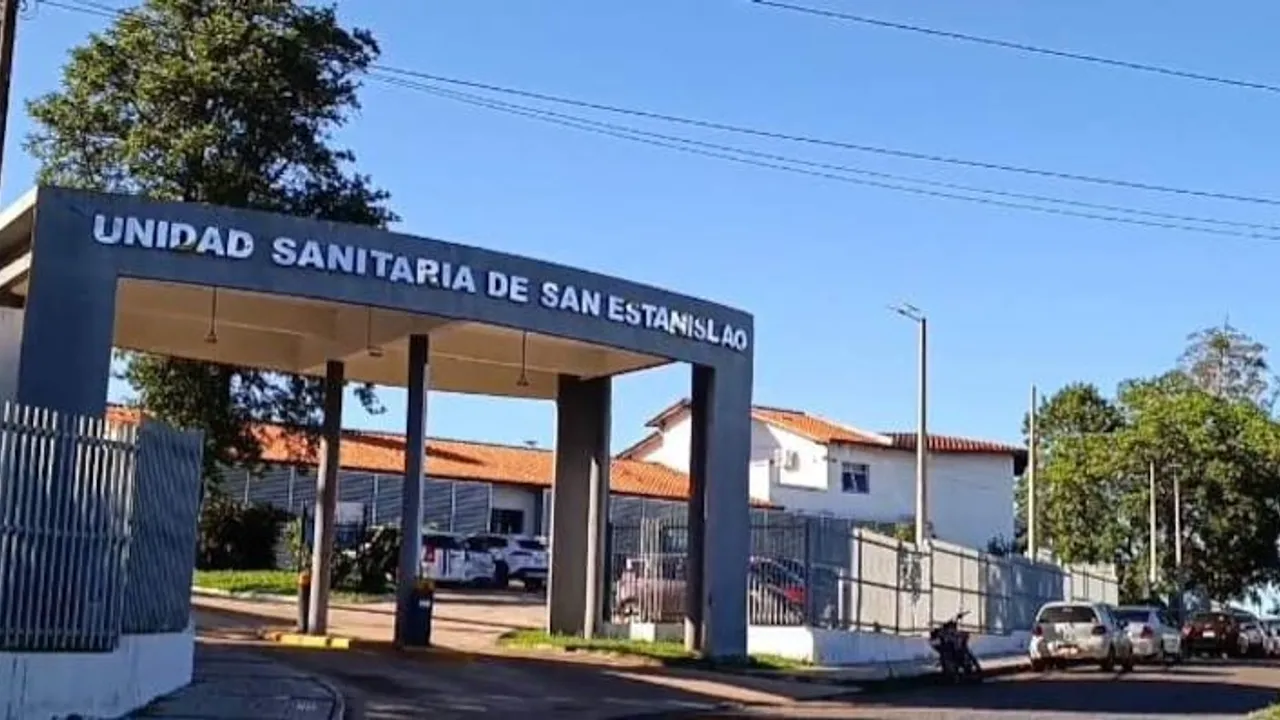 Pórtico de acceso y fachada de la Unidad Sanitaria de San Estanislao con rejas perimetrales bajo un cielo despejado.
