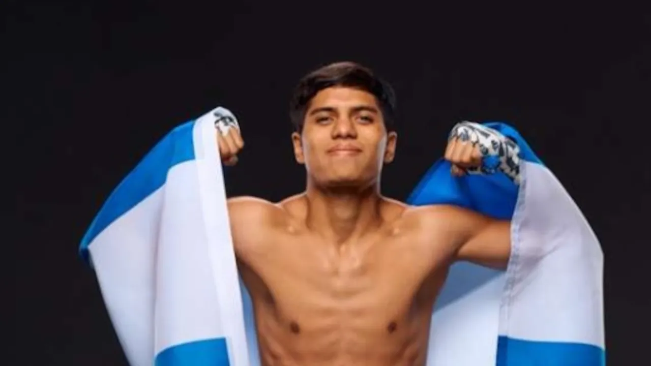 Boxeador joven sin camiseta sonríe y levanta los puños envueltos sosteniendo una bandera celeste y blanca