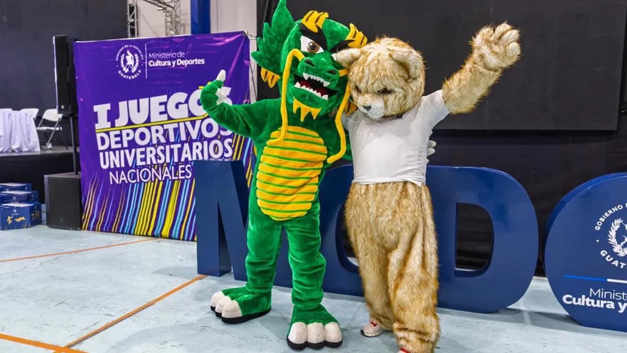 Dos botargas, una con figura de dragón verde y otra de felino claro, posan abrazadas en un escenario deportivo.