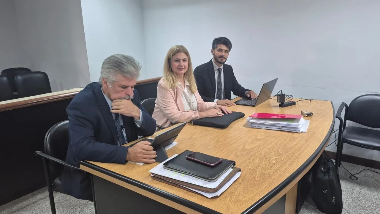 Arnaldo Giuzzio sentado junto a su abogada y un asistente técnico frente a documentos durante una audiencia judicial.