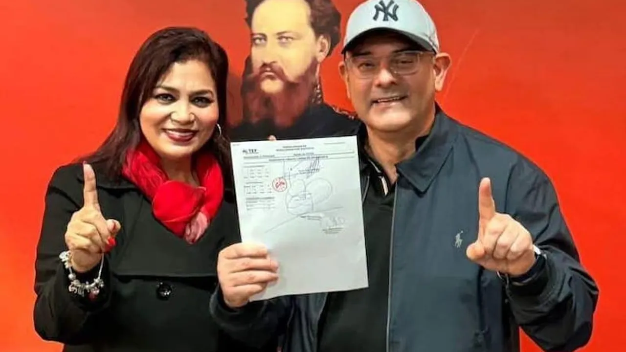 Un hombre con gorra y lentes y una mujer con bufanda roja muestran un documento oficial con sellos sobre fondo rojo.