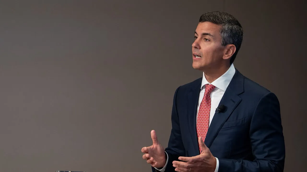 Santiago Peña con traje oscuro y corbata roja gesticula mientras expone de pie en un evento institucional